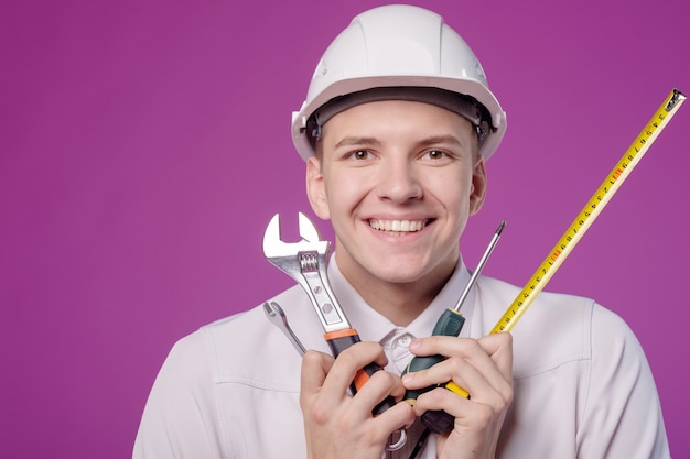 Jeune homme en casque blanc avec outil de travail à la main sur fond violet