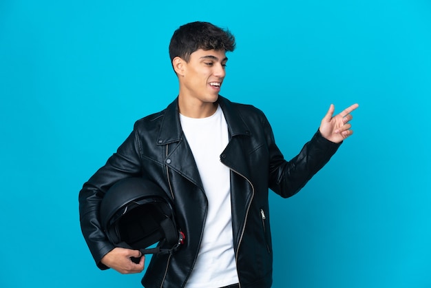 Jeune homme avec un casque de moto sur le doigt pointé bleu sur le côté et présentant un produit