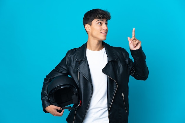 Jeune homme avec un casque de moto sur fond bleu isolé pointant vers le haut une excellente idée