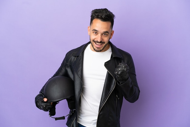 Jeune homme avec un casque de moto isolé sur fond violet célébrant une victoire en position de vainqueur