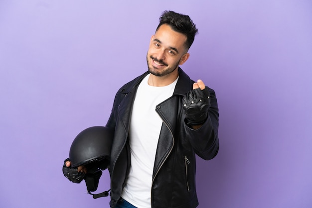 Jeune homme avec un casque de moto isolé sur fond violet faisant un geste d'argent