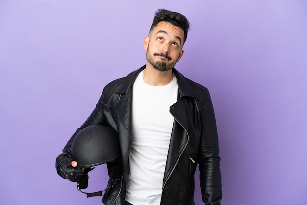 Jeune homme avec un casque de moto isolé sur fond violet et levant