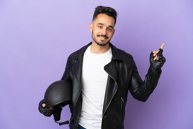 Jeune homme avec un casque de moto isolé sur fond violet montrant et levant un doigt en signe du meilleur