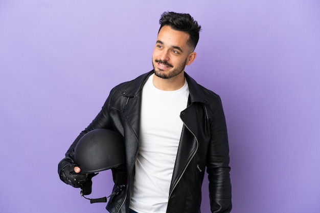 Jeune homme avec un casque de moto isolé sur fond violet regardant sur le côté et souriant