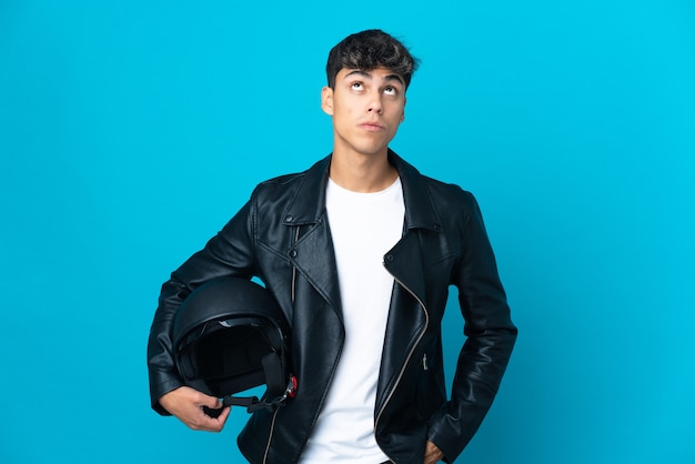 Jeune homme avec un casque de moto sur un mur bleu isolé à la recherche et avec une expression de surprise