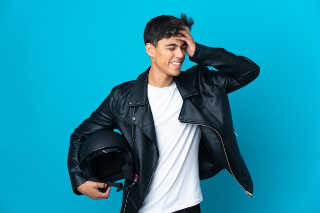 Jeune homme avec un casque de moto sur un mur bleu isolé souriant beaucoup