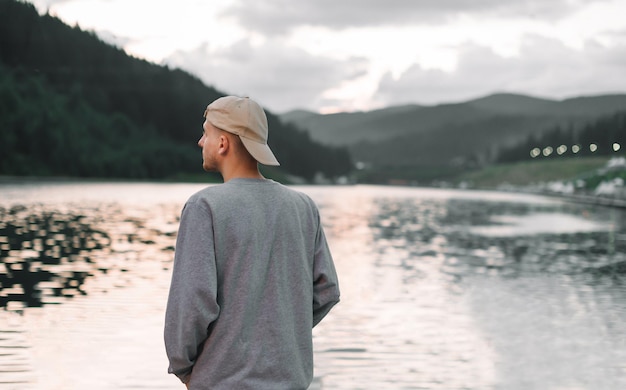 Un jeune homme en casquette se tient sur le lac dans les montagnes et regarde le magnifique paysage