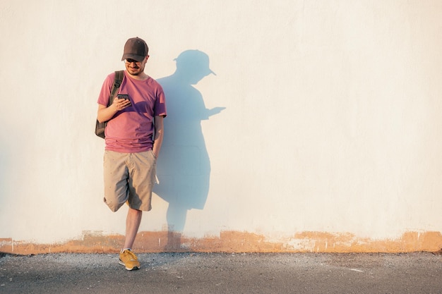 Jeune homme avec une casquette et un téléphone portable sourit sur un fond blanc dans la rue