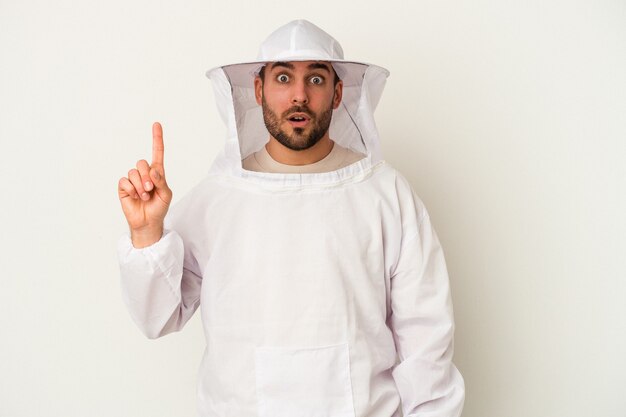 Jeune homme caucasien d'apiculture isolé sur fond blanc ayant une bonne idée, concept de créativité.