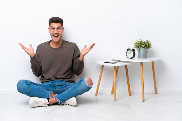 Jeune homme caucasien assis dans sa maison isolé sur fond blanc avec une expression faciale choquée