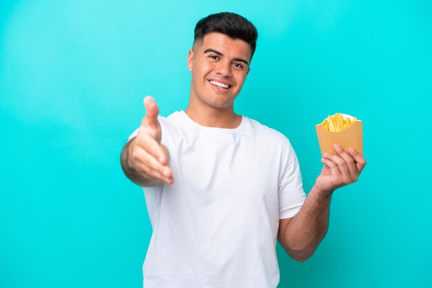 Jeune homme caucasien attrapant des frites isolées sur fond bleu se serrant la main pour conclure une bonne affaire