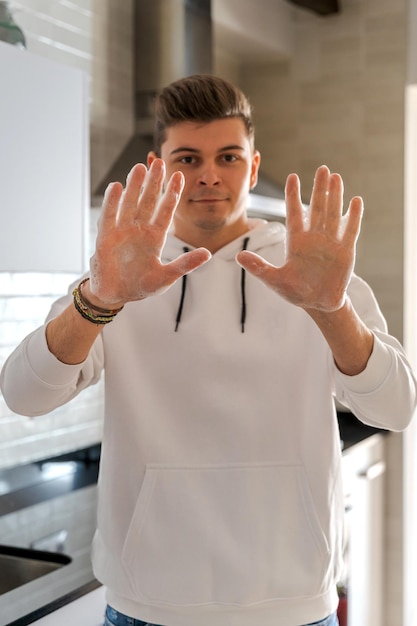 Jeune homme caucasien aux mains savonneuses Il regarde la caméra Il est jeune et porte un sweat-shirt Dans la cuisine avec lumière naturelle en Espagne