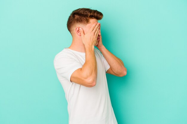 Jeune Homme Caucasien Sur Bleu Peur Couvrant Les Yeux Avec Les Mains.