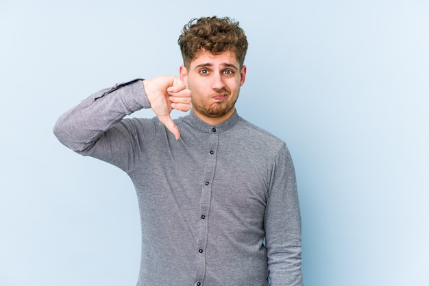 Jeune homme caucasien blond cheveux bouclés isolé montrant le pouce vers le bas, concept de déception.