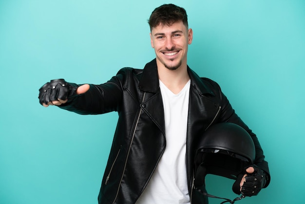 Jeune homme caucasien avec un casque de moto isolé sur fond bleu donnant un geste du pouce levé