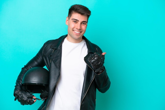 Jeune homme caucasien avec un casque de moto isolé sur fond bleu pointant vers le côté pour présenter un produit