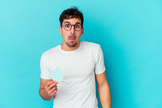 Jeune homme caucasien célébrant la journée mondiale de l'eau isolée hausse les épaules et les yeux ouverts confus.