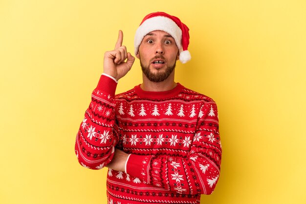 Jeune homme caucasien célébrant Noël isolé sur fond jaune ayant une bonne idée, concept de créativité.