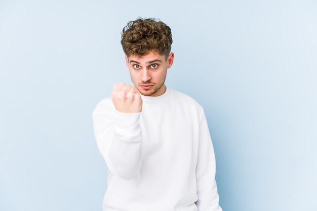 Jeune homme caucasien cheveux bouclés blonds isolé montrant le poing à la caméra, une expression faciale agressive.