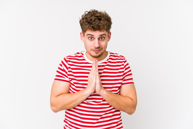 Jeune homme caucasien cheveux bouclés blonds isolé priant, montrant la dévotion, personne religieuse à la recherche d'inspiration divine.