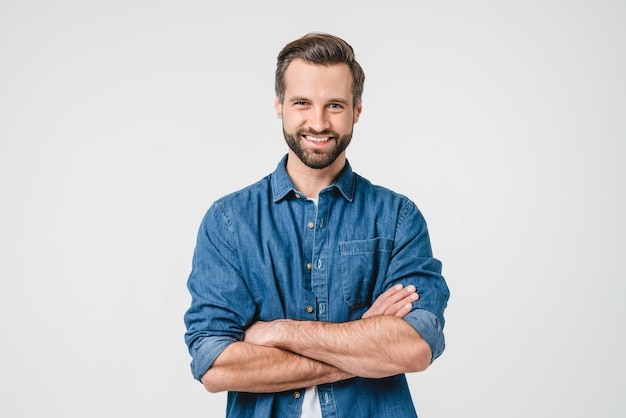 Jeune homme caucasien confiant en vêtements de denim décontractés avec les bras croisés regardant la caméra avec un sourire denté isolé sur un fond blanc