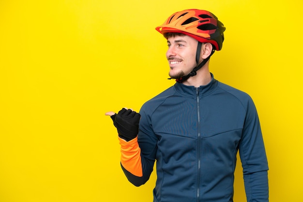 Jeune homme caucasien cycliste isolé sur fond jaune pointant vers le côté pour présenter un produit