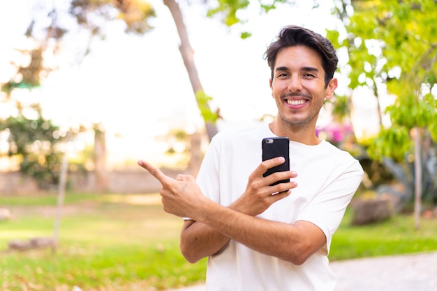 Jeune homme caucasien dans un parc à l'aide de téléphone portable et pointant vers l'arrière