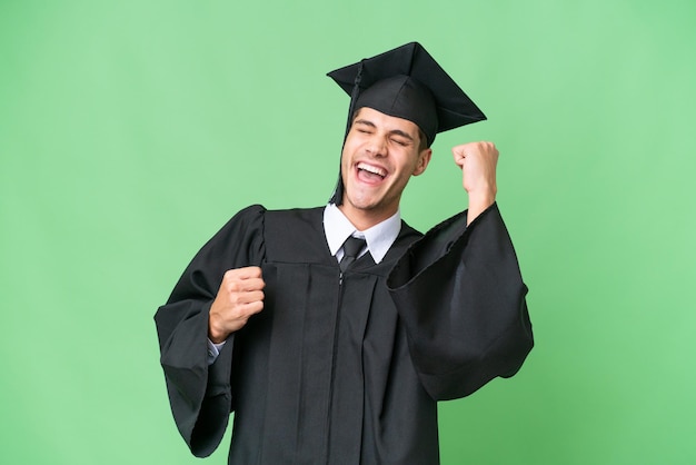 Jeune homme caucasien diplômé universitaire sur fond isolé célébrant une victoire