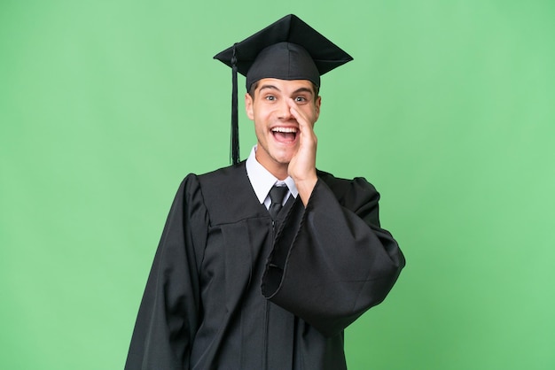 Jeune homme caucasien diplômé universitaire sur fond isolé criant avec la bouche grande ouverte