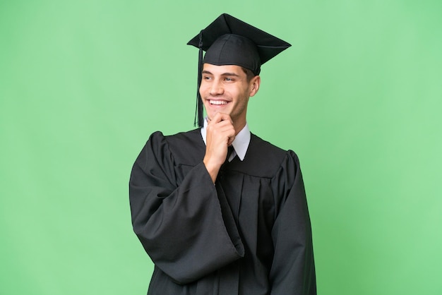 Jeune homme caucasien diplômé universitaire sur fond isolé regardant sur le côté