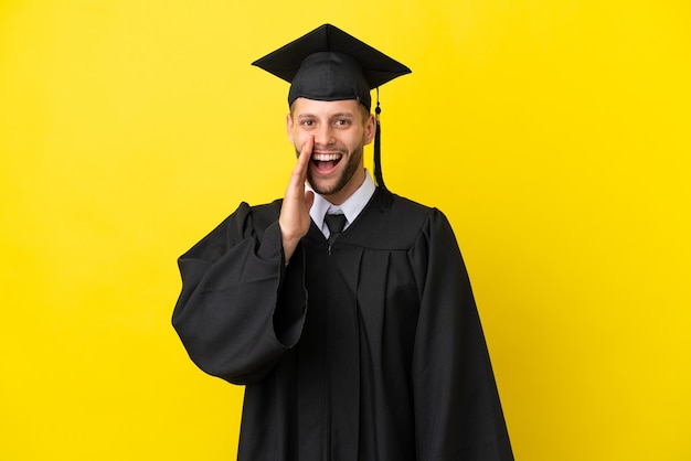 Jeune homme caucasien diplômé universitaire isolé sur fond jaune avec une expression faciale surprise et choquée