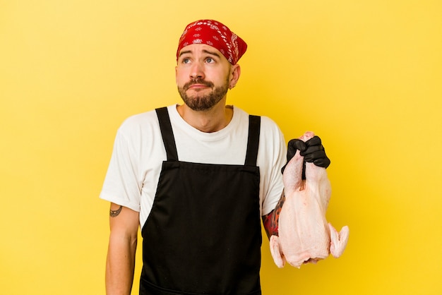 Jeune homme caucasien doseur tatoué tenant un poulet isolé sur mur jaune rêvant d'atteindre les objectifs et les fins