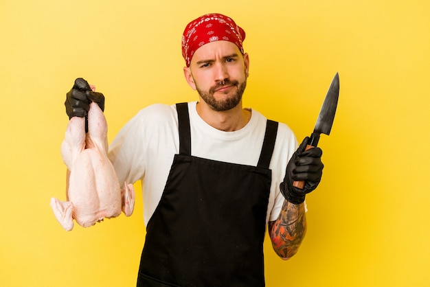 Jeune homme caucasien doseur tatoué tenant un poulet isolé sur mur jaune