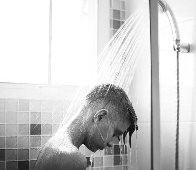 Jeune homme caucasien douche dans la salle de bain en niveaux de gris