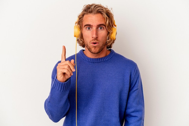 Jeune homme caucasien écoutant de la musique isolé sur fond blanc ayant une bonne idée, concept de créativité.