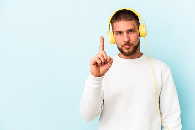 Jeune homme caucasien écoutant de la musique isolée sur fond bleu montrant le numéro un avec le doigt.