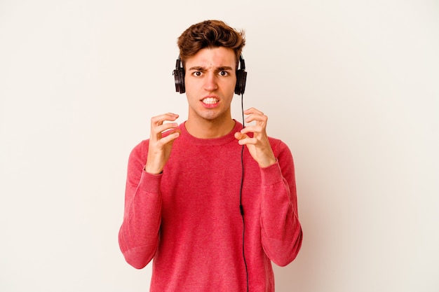 Jeune homme caucasien, écouter de la musique sur blanc bouleversé criant avec des mains tendues.