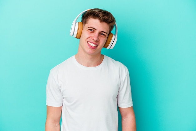 Jeune homme caucasien, écouter de la musique avec un casque isolé sur fond bleu heureux, souriant et joyeux.