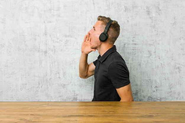 Jeune homme caucasien, écouter de la musique avec des écouteurs en criant et en tenant la paume près de la bouche ouverte.