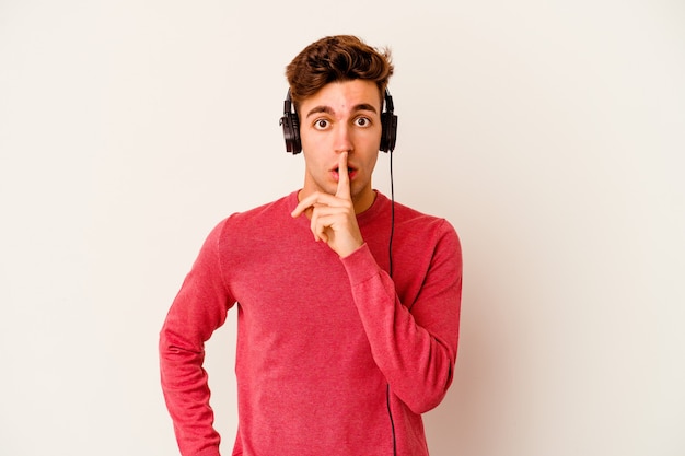 Jeune homme caucasien, écouter de la musique isolé sur fond blanc en gardant un secret ou en demandant le silence.