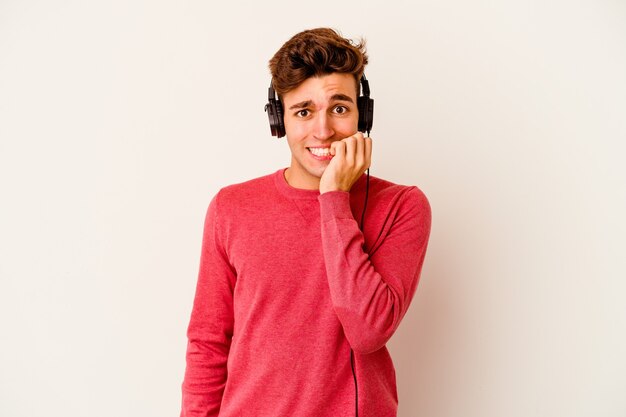 Jeune homme caucasien, écouter de la musique isolée sur fond blanc, se ronger les ongles, nerveux et très anxieux.