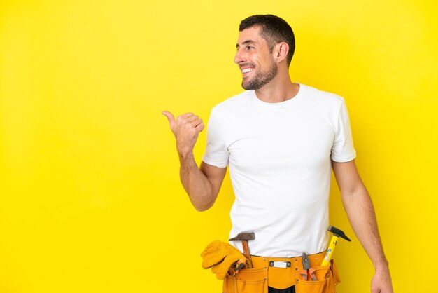 Jeune homme caucasien électricien isolé sur fond jaune pointant vers le côté pour présenter un produit