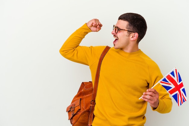 Jeune homme caucasien étudiant l'anglais isolé sur un mur blanc levant le poing après une victoire, concept gagnant.