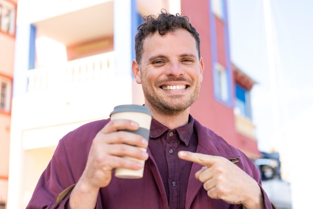 Jeune homme caucasien à l'extérieur tenant un café à emporter avec une expression heureuse