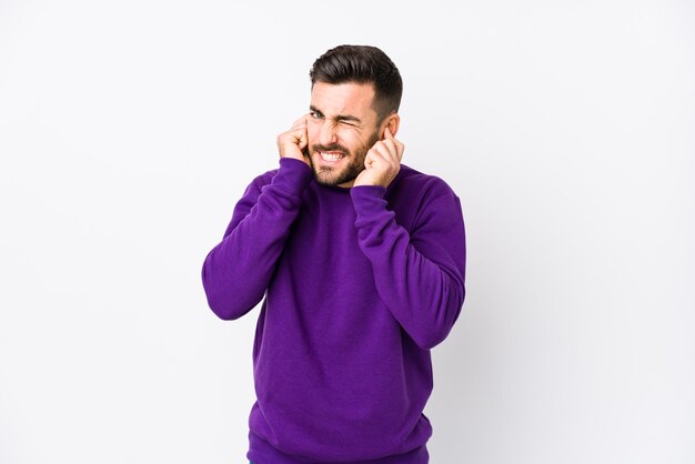 Jeune homme caucasien sur fond blanc isolé couvrant les oreilles avec les mains.