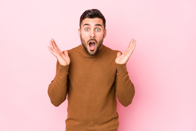 Jeune homme caucasien sur fond rose isolé surpris et choqué.