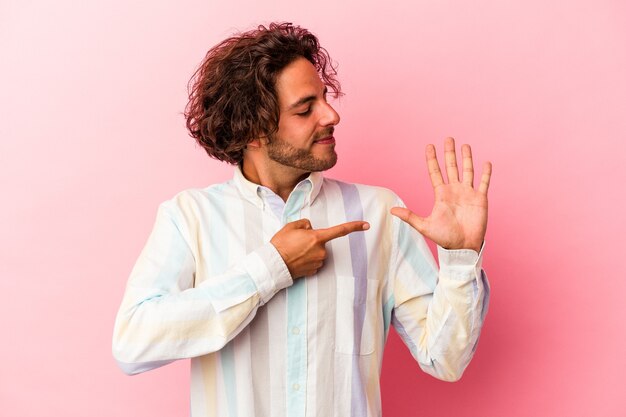 Jeune homme caucasien isolé sur bakcground rose souriant joyeux montrant le numéro cinq avec les doigts.