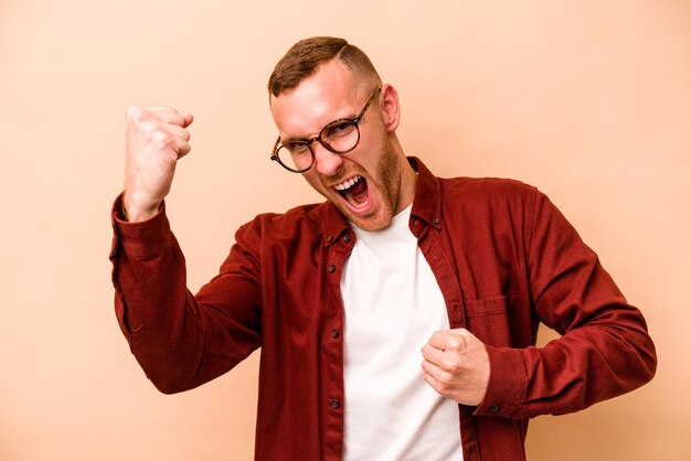 Jeune homme caucasien isolé sur fond beige acclamant le concept de victoire insouciant et excité