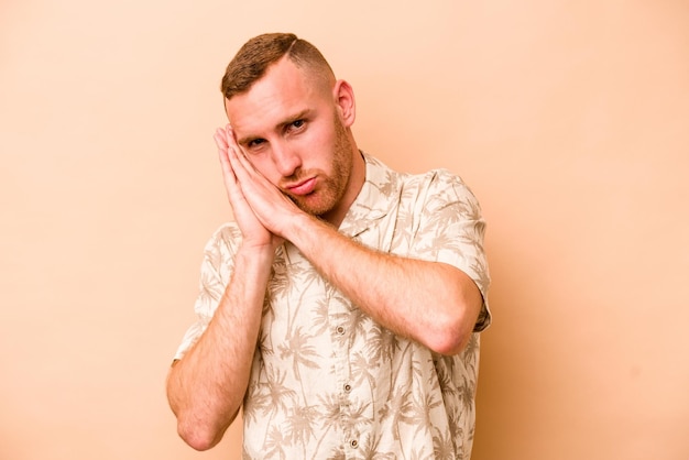 Jeune homme caucasien isolé sur fond beige bâillant montrant un geste fatigué couvrant la bouche avec la main