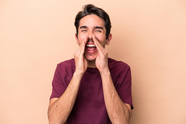 Jeune homme caucasien isolé sur fond beige disant un potin, pointant vers le côté rapportant quelque chose.